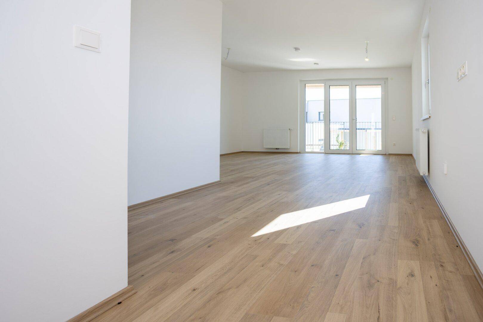 Lichtdurchfluteter Wohnbereich mit hellem Laminatboden und großzügigem Zugang zum Außenbereich.