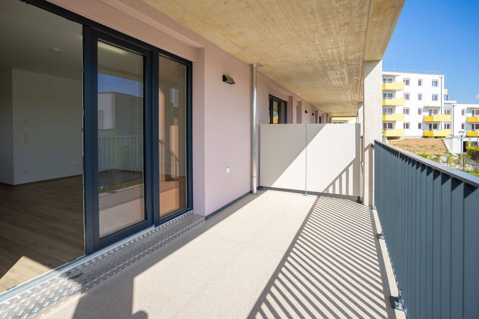 Langer Balkon mit Schiebetüren zum Innenraum und Blick auf die umliegenden Gebäude.