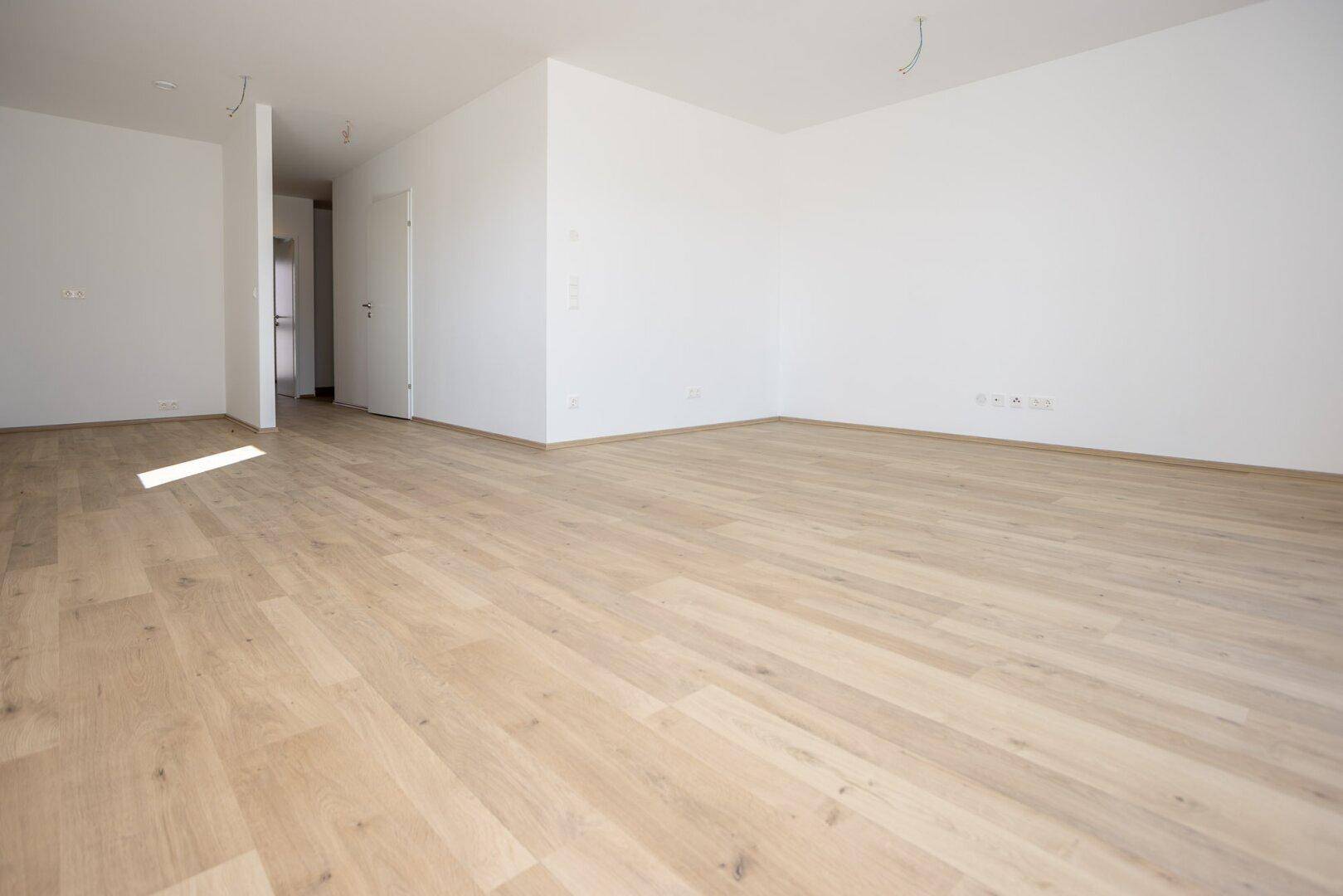 Geräumiger, leerer Wohnbereich mit hellem Laminatboden und Zugang zu weiteren Räumen.