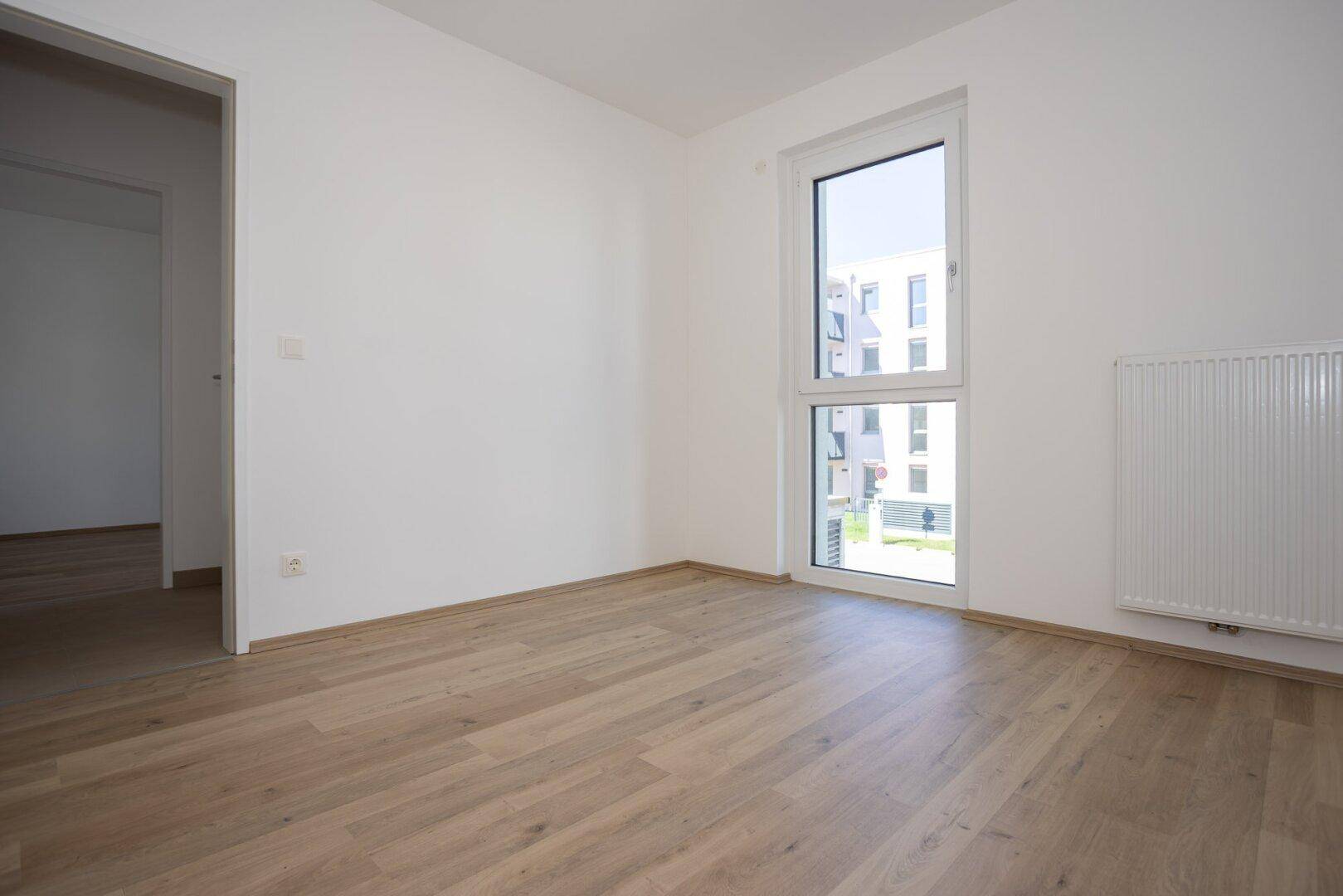 Geräumiges Schlafzimmer mit hellem Laminatboden, weißen Wänden und Blick auf die Umgebung.
