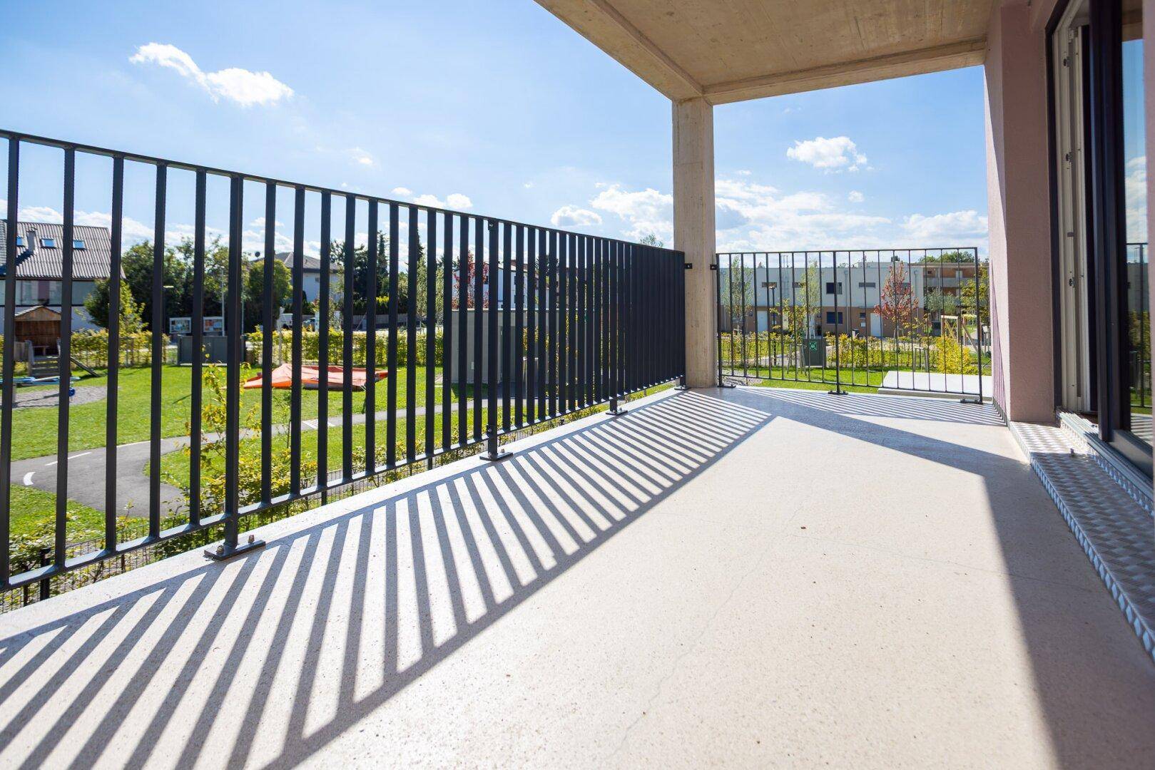 Sonniger Balkon mit Metallgeländer und weitem Blick über die grüne Umgebung.