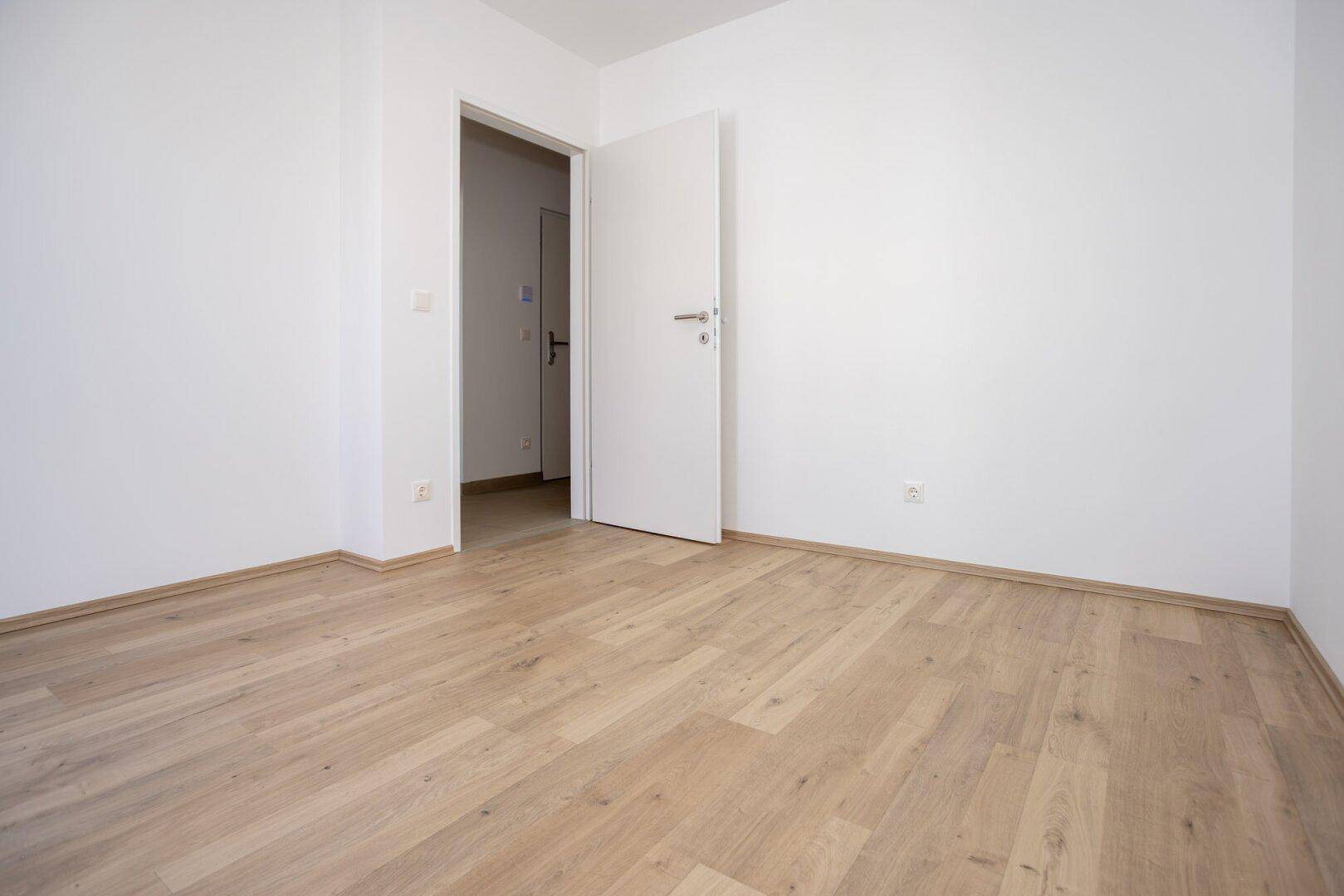 Leeres Schlafzimmer mit hellem Laminatboden und weiß gestrichenen Wänden, bereit zur Einrichtung.
