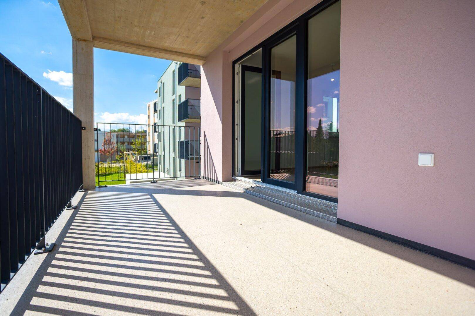 Heller Balkon mit Zugang zum Innenraum und Blick auf die moderne Wohnanlage.