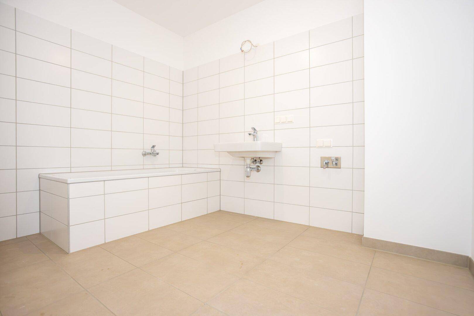 Modernes Badezimmer mit weißen Fliesen, beigem Boden und einer eingebauten Badewanne.