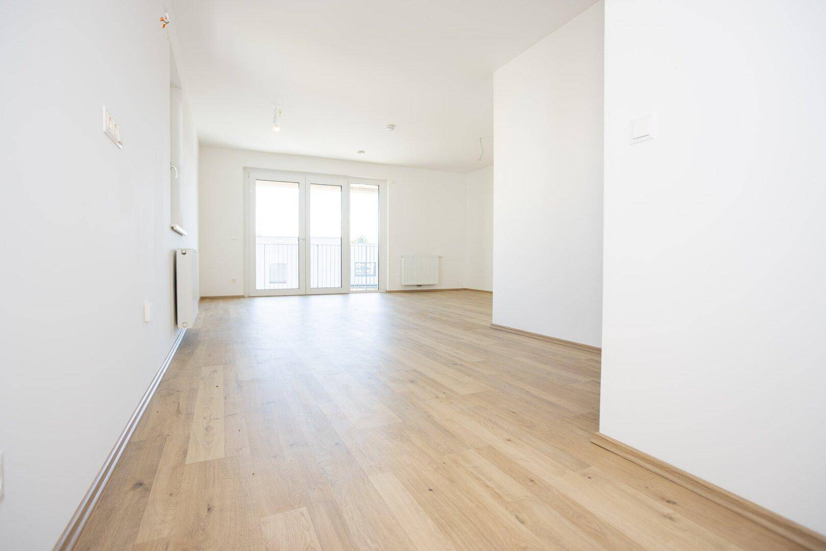 Geräumiges, unmöbliertes Zimmer mit Laminatboden und viel Tageslicht durch die Balkontür.