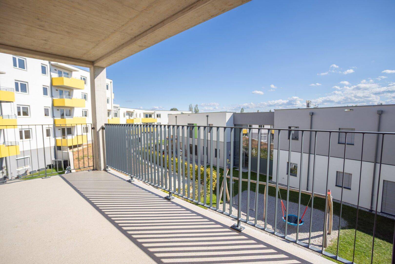 Geräumiger Balkon mit Betonboden und Metallgeländer, Blick auf den Innenhof und Spielplatz.