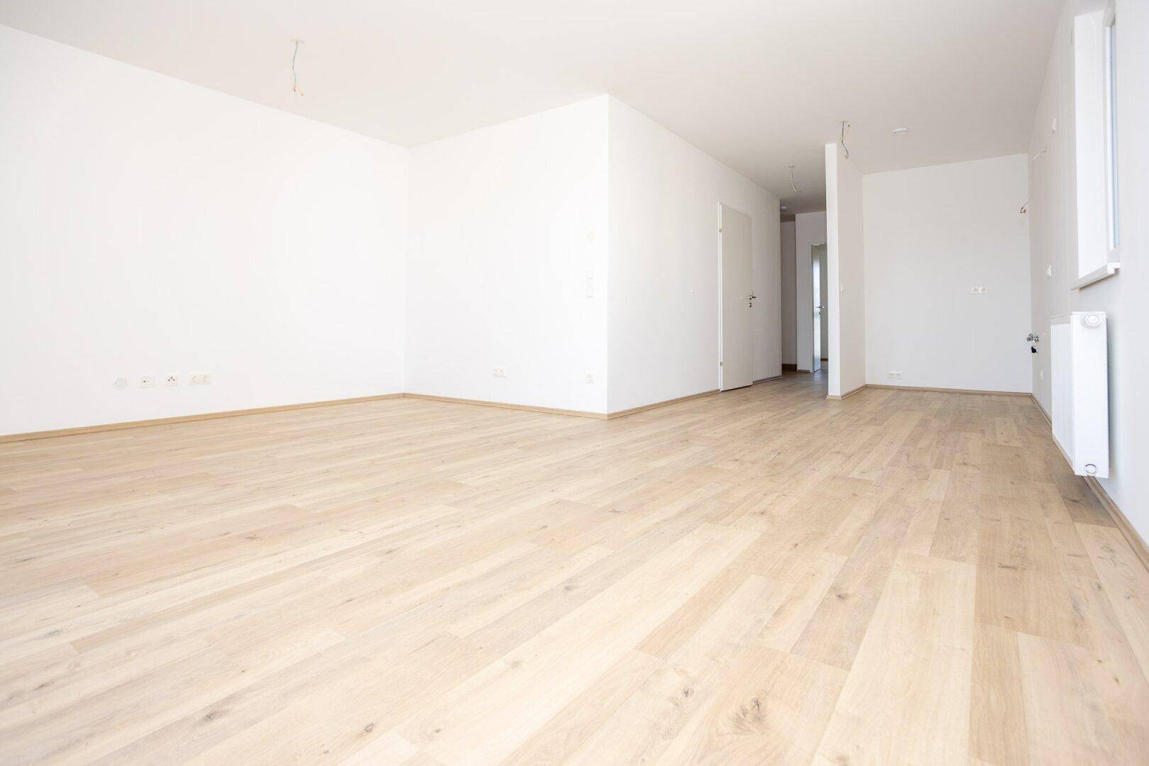 Heller, leerer Raum mit modernem Laminatboden und weiß gestrichenen Wänden.