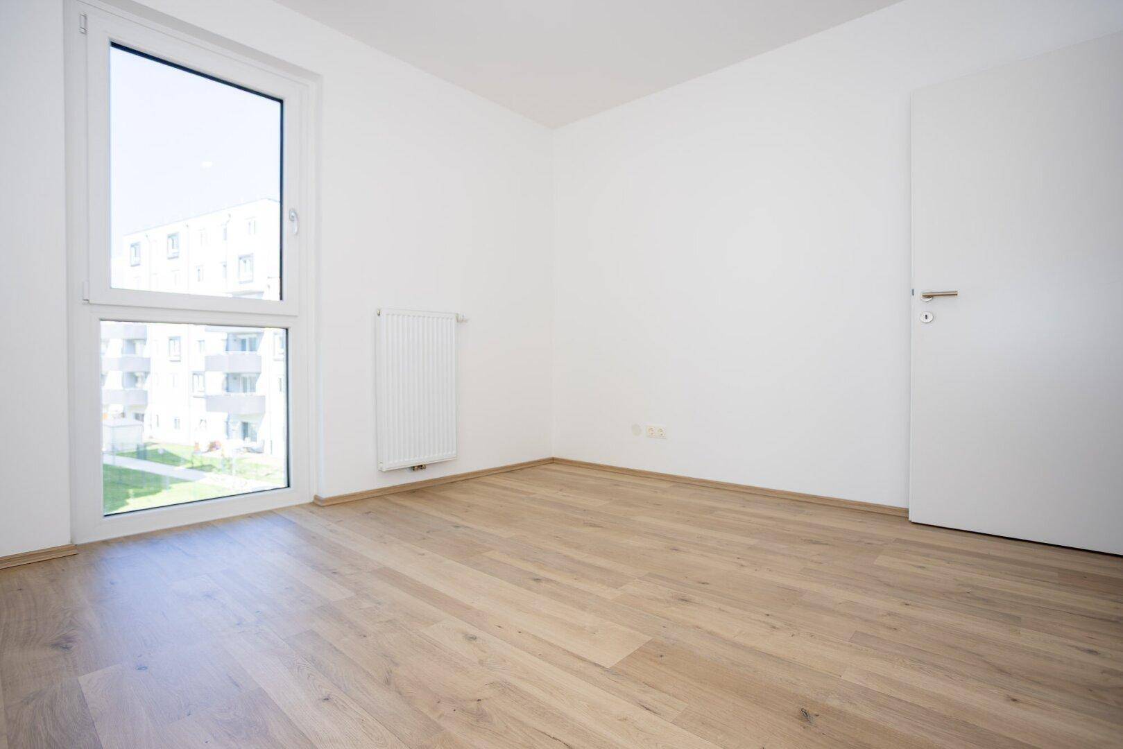Unmöbliertes Schlafzimmer mit hellem Laminatboden und weiß gestrichenen Wänden.