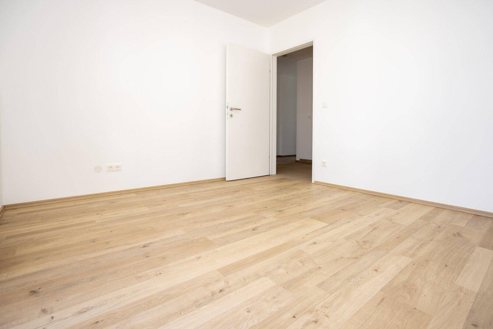Leeres Zimmer mit Laminatboden und weißer Tür, bereit zur individuellen Gestaltung.