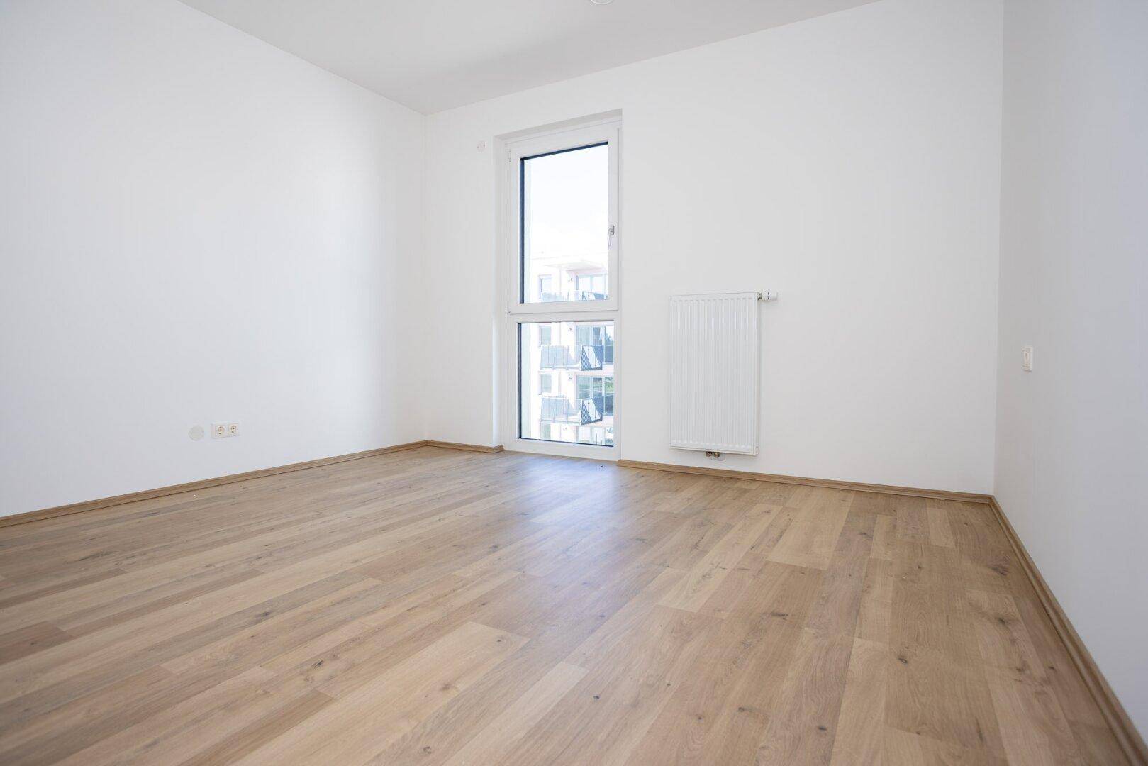 Unmöbliertes Zimmer mit hellem Laminatboden und Fenster, das viel Tageslicht bietet.