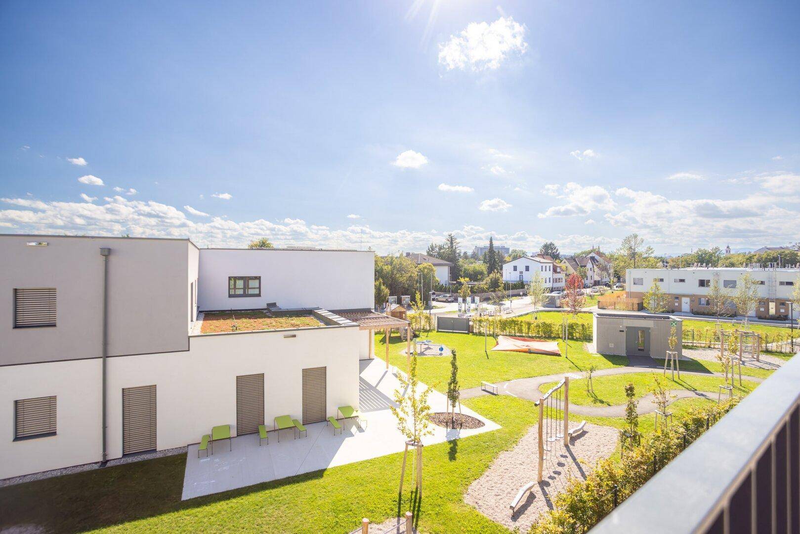 Weitläufiger grüner Innenhof mit Spielplatz und modernen Wohngebäuden unter blauem Himmel.