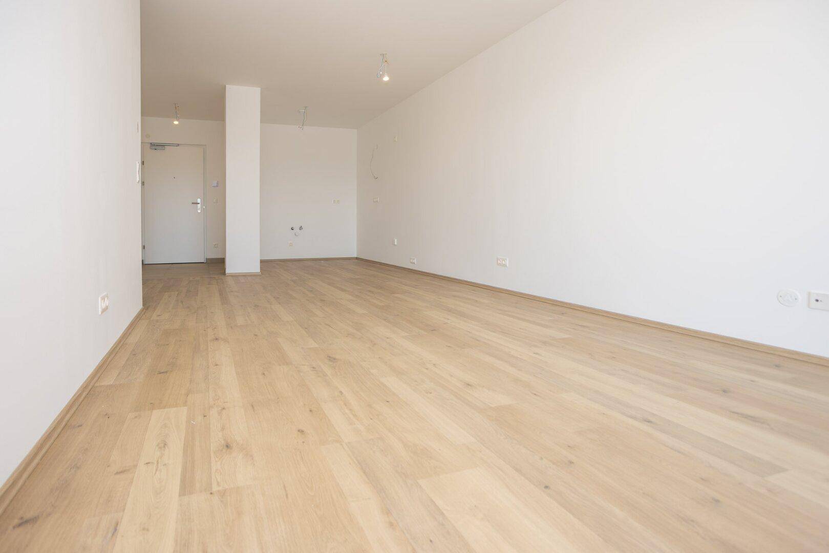 Leerer Wohnraum mit hellen Laminatböden und weißen Wänden, bereit für die Einrichtung.