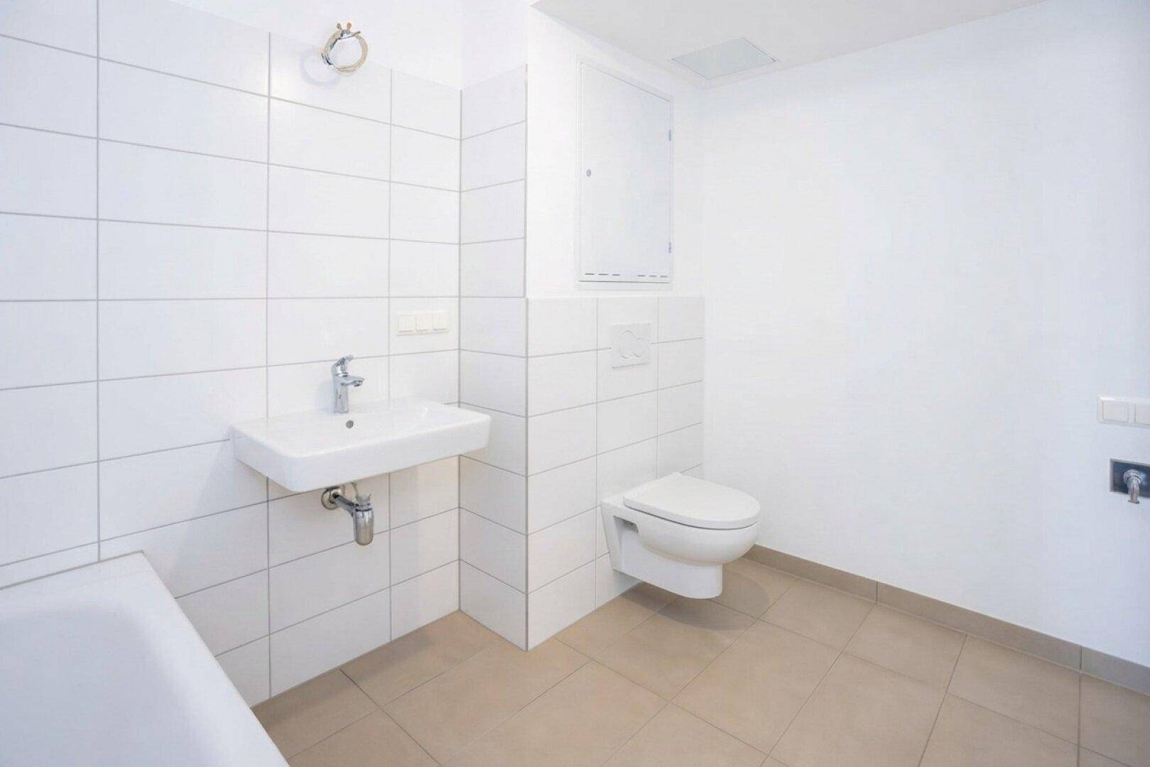 Modernes Badezimmer mit weißen Wandfliesen, Waschbecken, Toilette und beigen Bodenfliesen.