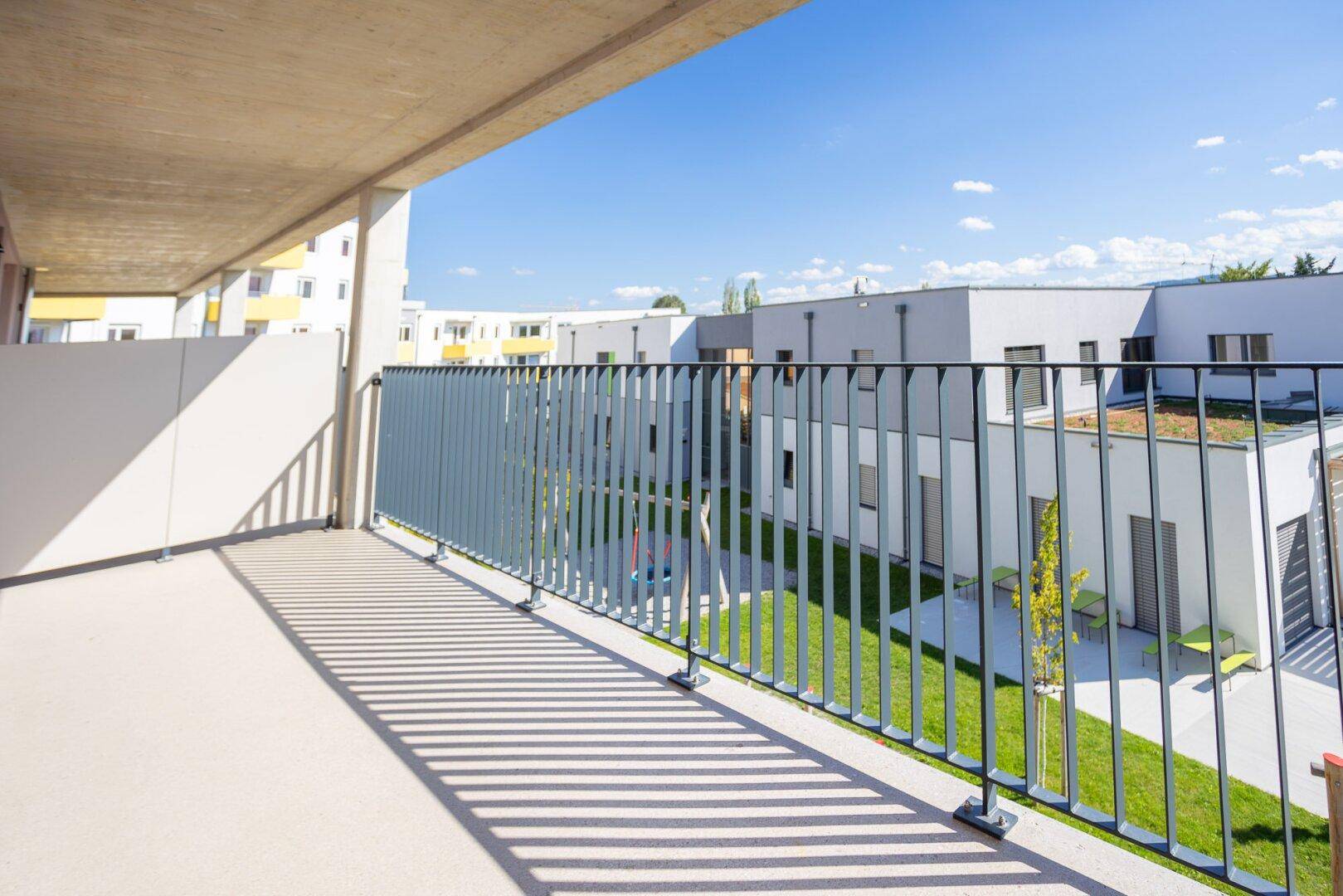 Heller Balkon mit Blick auf einen modernen Innenhof mit Grünflächen und zeitgenössischen Gebäuden.