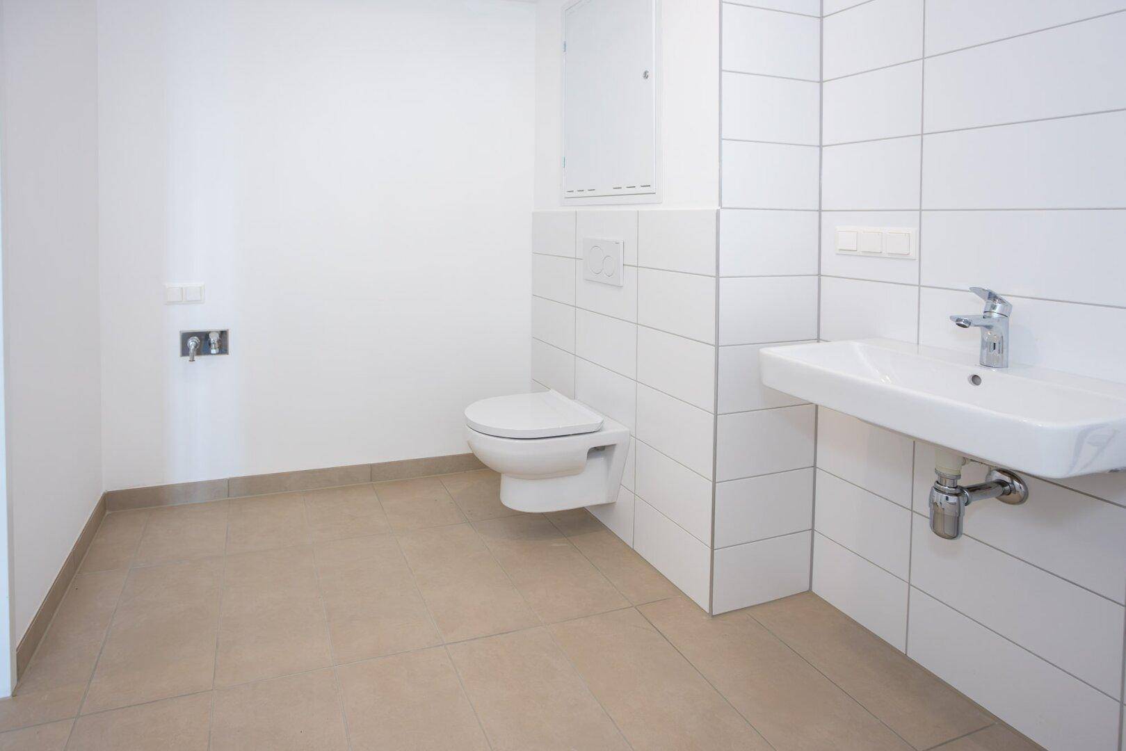 Modernes Badezimmer mit weißen Wandfliesen, beigefarbenem Boden und wandhängendem WC sowie Waschbecken.