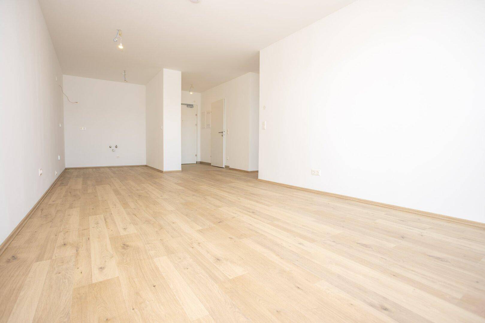 Geräumiger, leerer Raum mit hellem Holzboden und weißen Wänden, bereit zur individuellen Gestaltung.