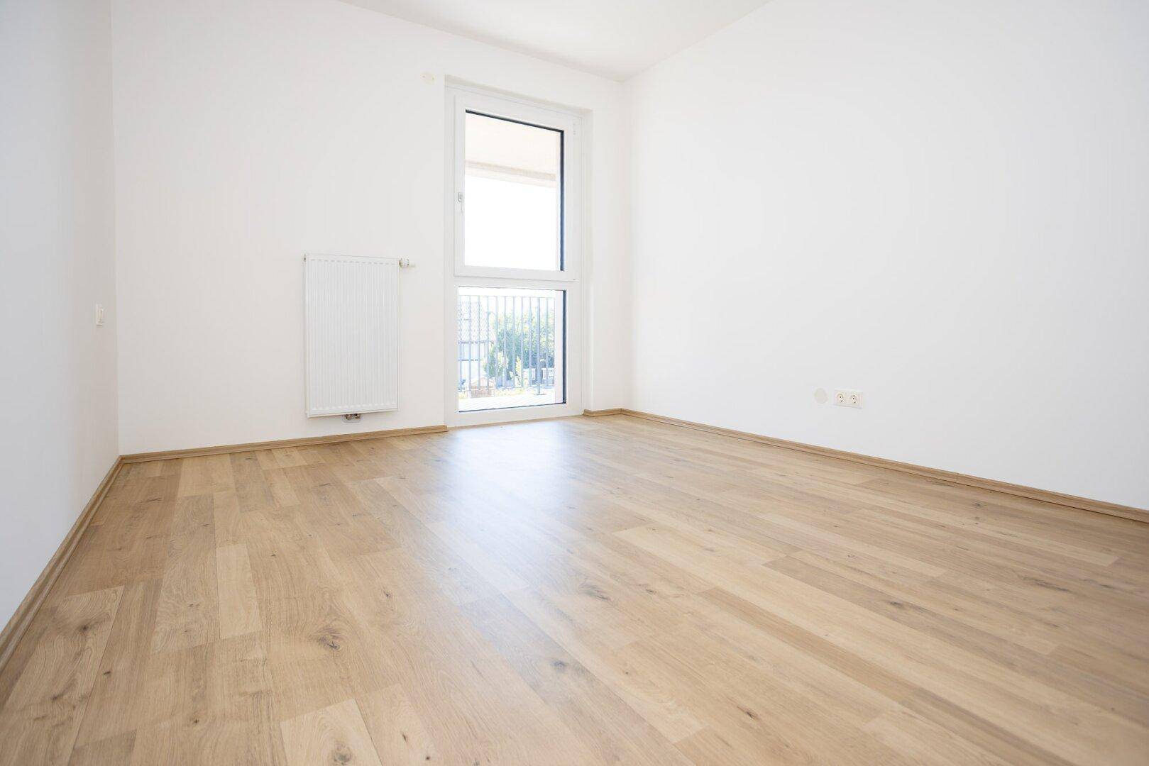 Freundliches Zimmer mit hellem Holzboden und großem Fenster, ideal als Schlaf- oder Arbeitszimmer.
