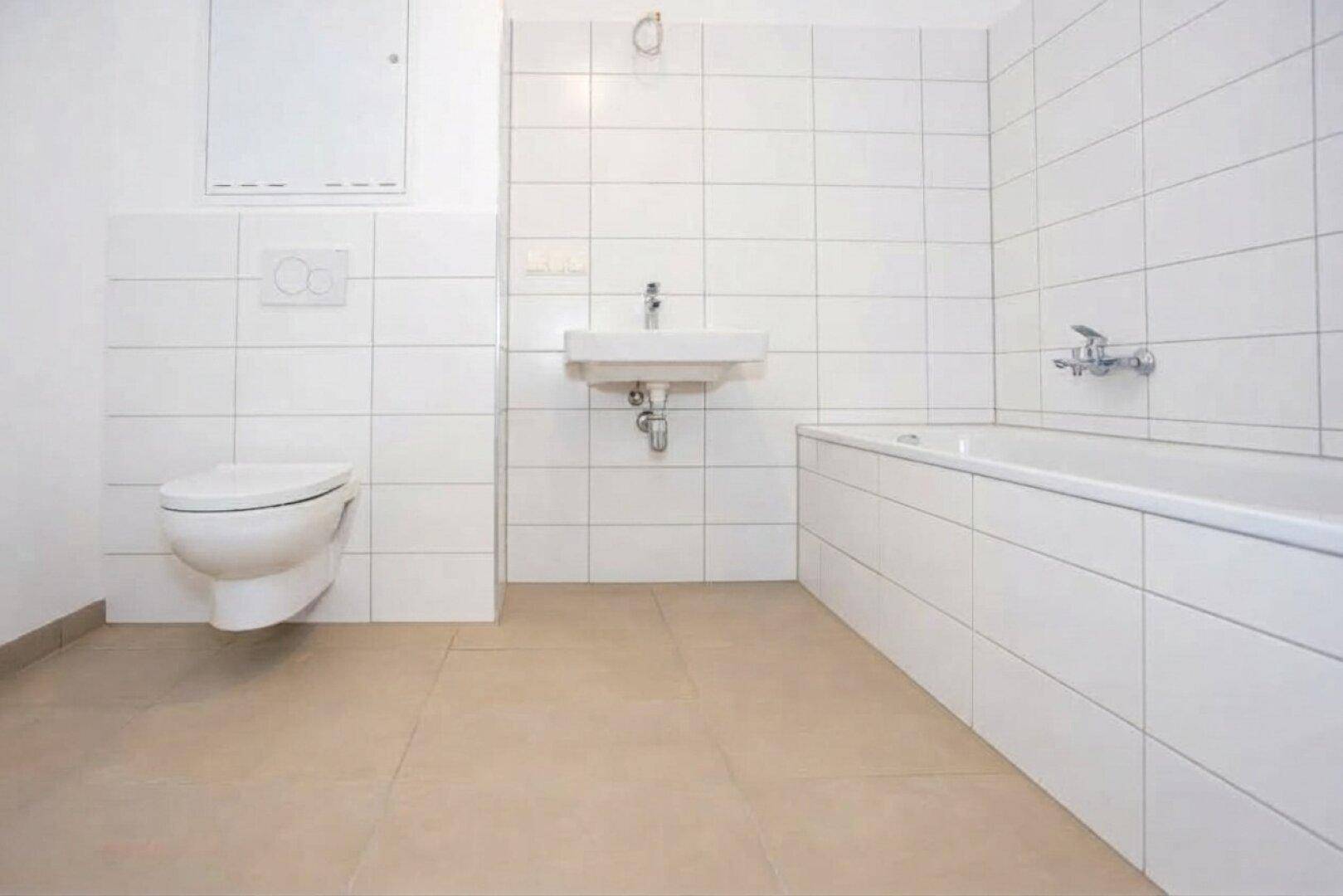 Helles Badezimmer mit Badewanne, wandhängendem WC und Waschbecken, ausgestattet mit weißen Fliesen.
