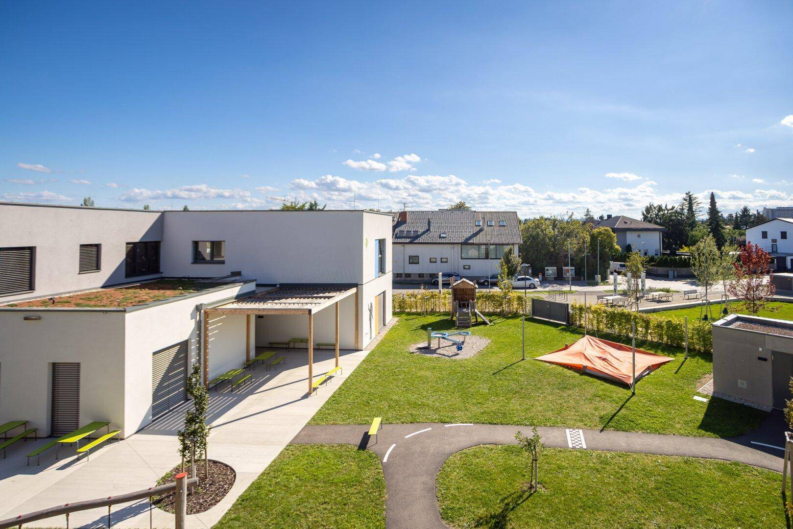 Weitläufiger Gemeinschaftsgarten mit Spielplatz und modernen Wohngebäuden unter blauem Himmel.