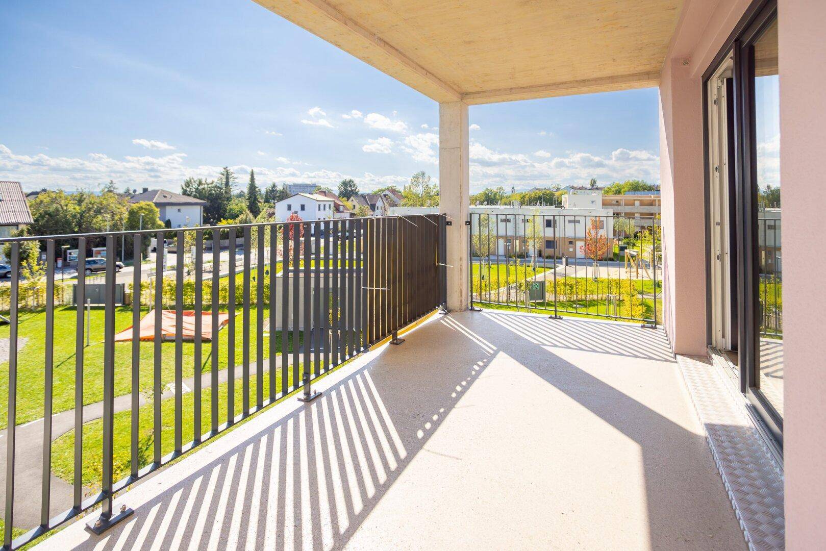 Heller Balkon mit Metallgeländer und Blick auf die grüne Umgebung und weitere Gebäude.
