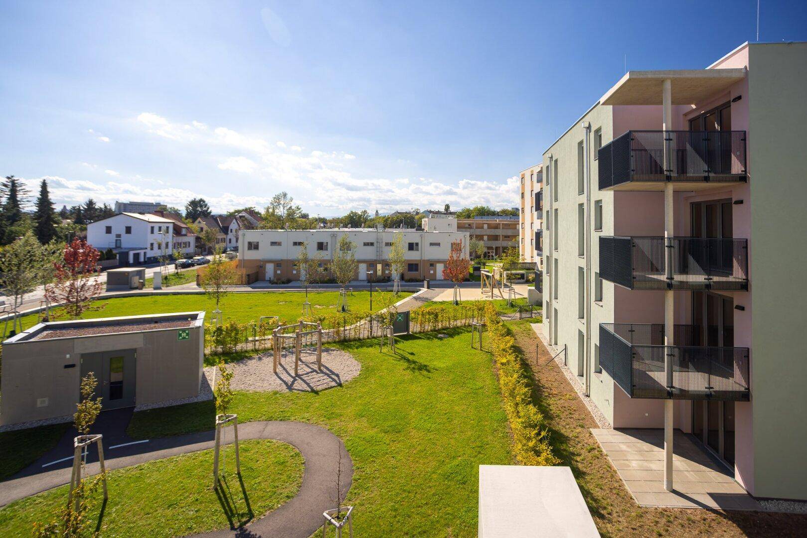 Gemeinschaftsgarten mit Spielplatz und modernen Wohngebäuden in einer sonnigen Umgebung.