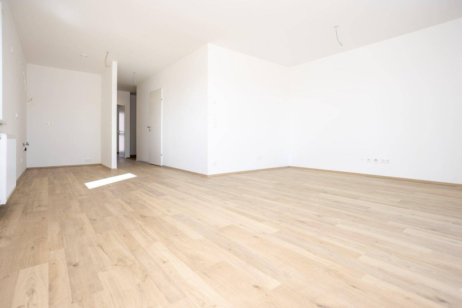 Offener Wohnbereich mit hellem Laminatboden und weißen Wänden, bereit zur individuellen Gestaltung.