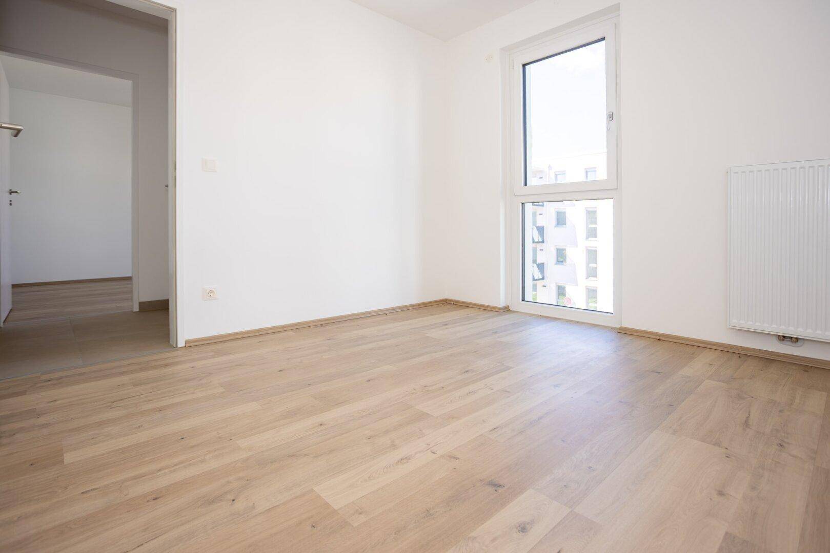 Geräumiges Schlafzimmer mit hellem Laminatboden und viel Tageslicht durch das Fenster.