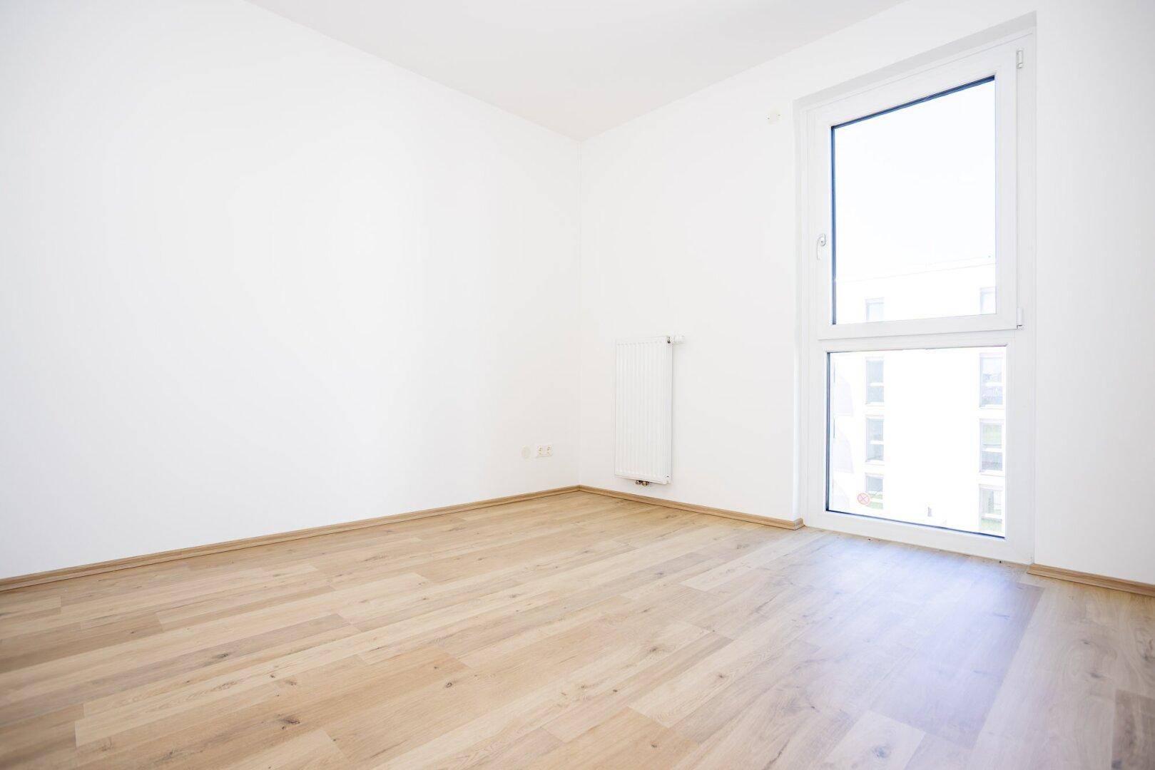 Freundliches Schlafzimmer mit Laminatboden und einem großen Fenster, das den Raum erhellt.