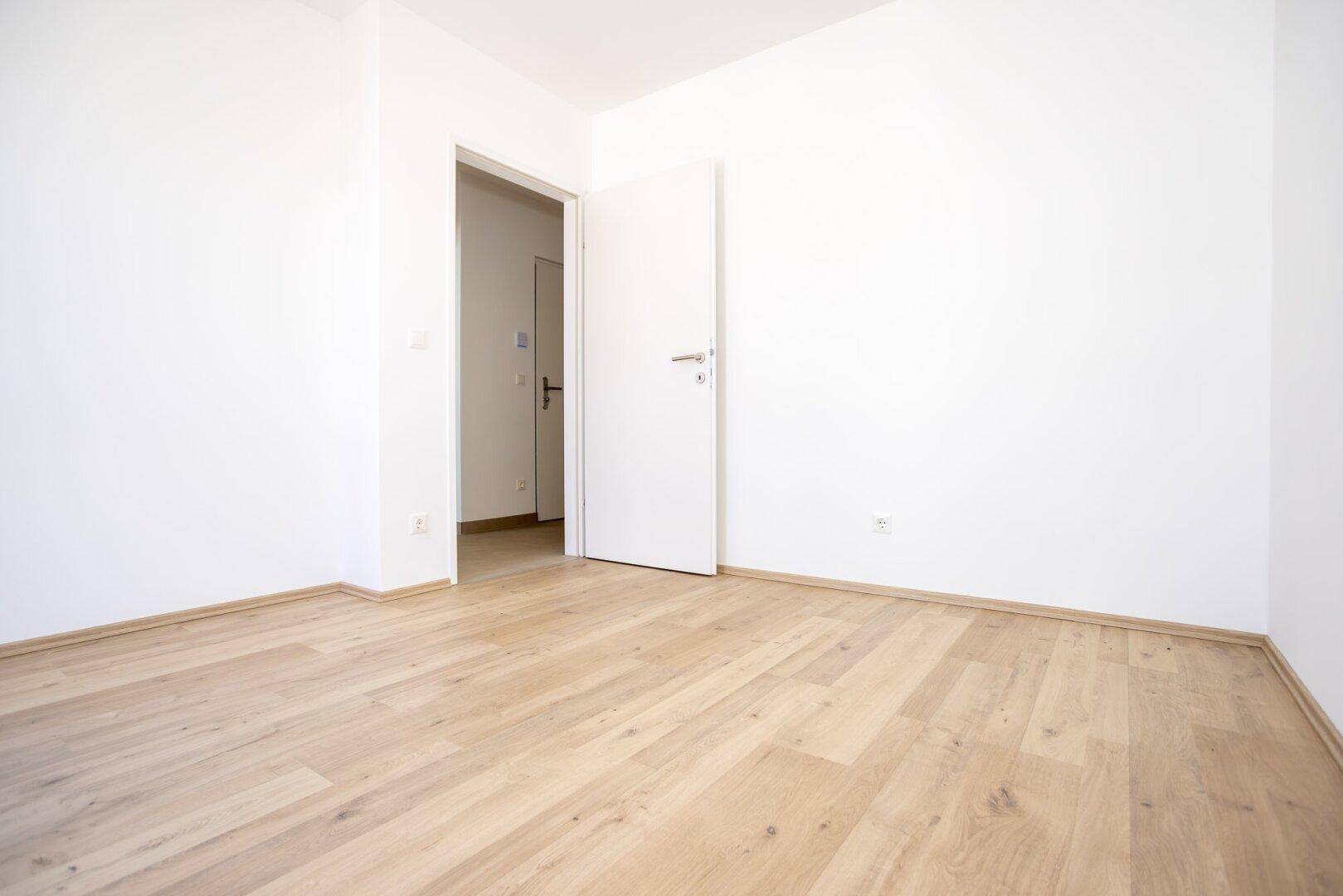 Geräumiges Schlafzimmer mit Laminatboden und weiß gestrichenen Wänden, bereit zur Einrichtung.