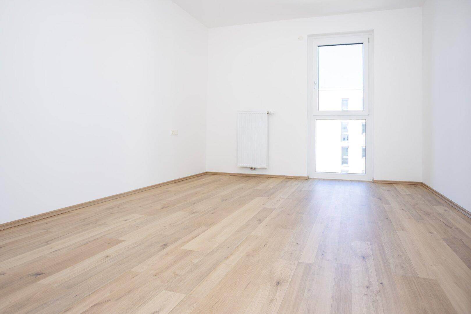 Freundliches Schlafzimmer mit Laminatboden und einem großen Fenster für viel Tageslicht.