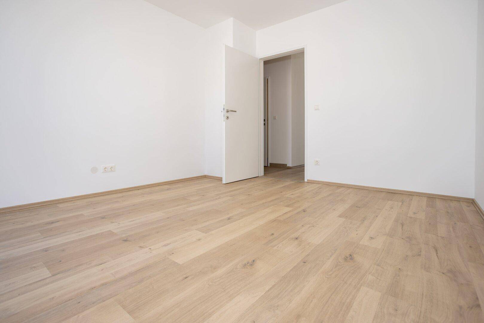 Geräumiges Schlafzimmer mit Laminatboden und weiß gestrichenen Wänden, bereit zur Einrichtung.