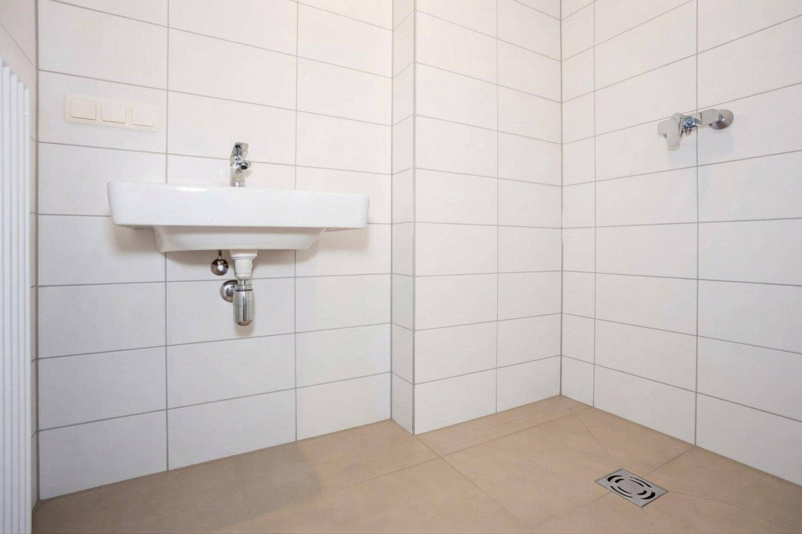 Modernes Badezimmer mit weißen Fliesen, Einzelwaschbecken und einer ebenerdigen Dusche.