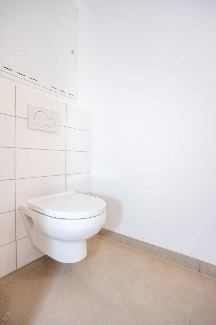 Separates WC mit wandhängender Toilette und weißen Fliesen, in modernem Design.