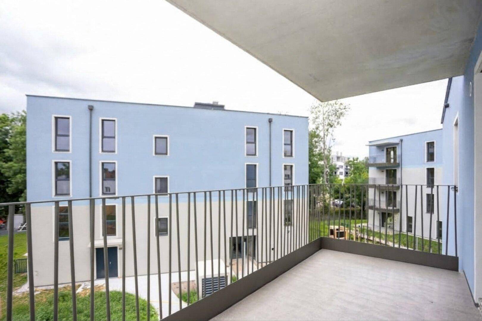 Blick vom Balkon auf moderne Wohngebäude mit blauer Fassade und umliegenden Grünflächen.