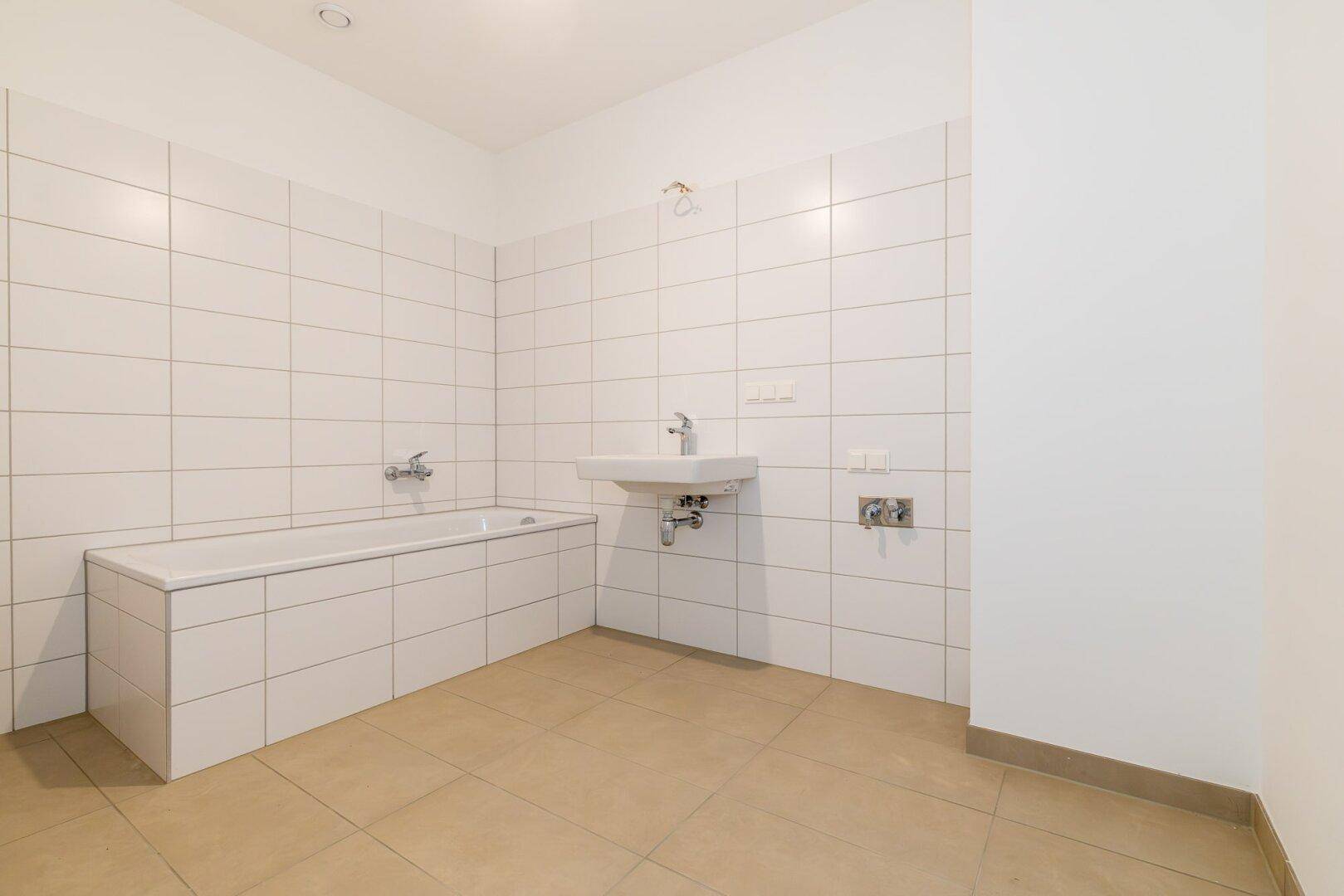 Modernes Badezimmer mit weißen Fliesen, Badewanne und Waschbecken, bereit zur Nutzung.