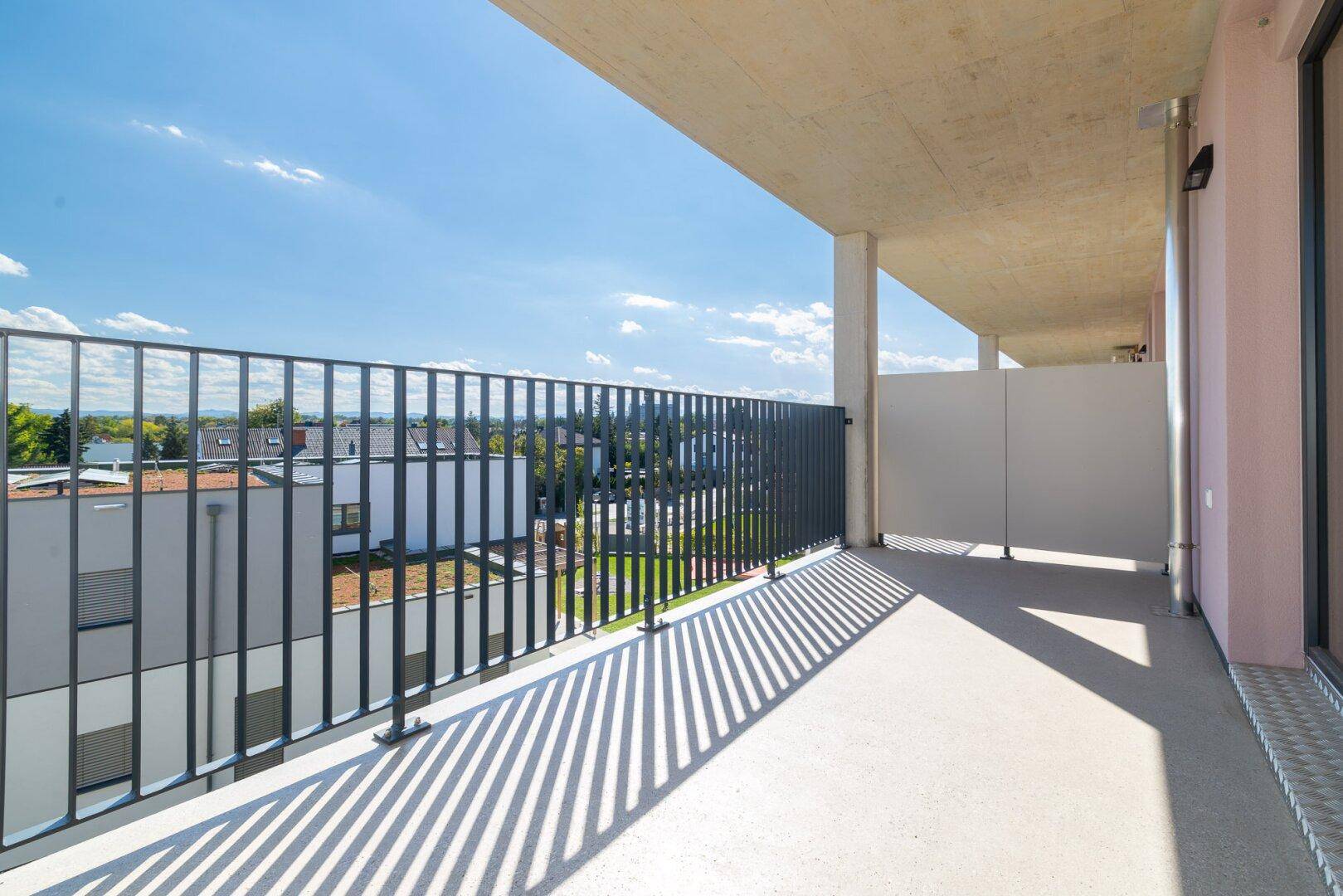 Langer Balkon mit seitlichem Sichtschutz und weitem Blick über die Umgebung an einem sonnigen Tag.