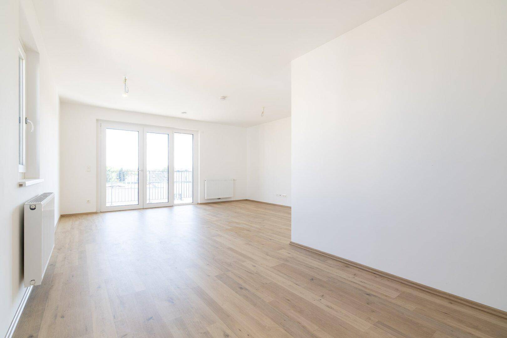 Helles, leeres Wohnzimmer mit Laminatboden und Zugang zu einem französischen Balkon.