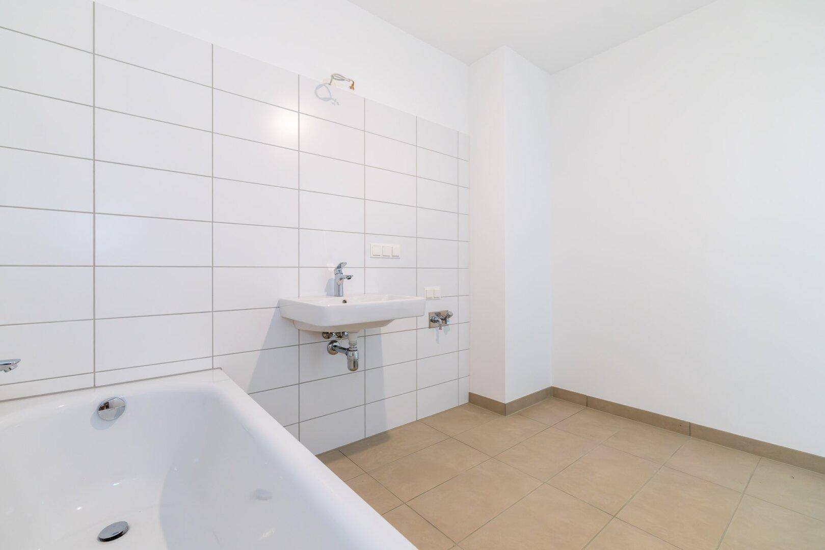 Helles Badezimmer mit weißen Wandfliesen, Badewanne und Waschbecken in minimalistischem Design.