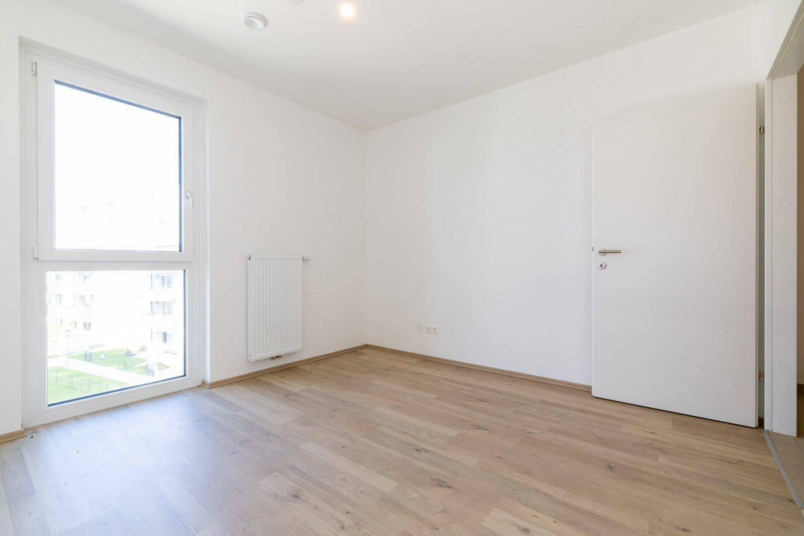 Freundliches Schlafzimmer mit Laminatboden und weißer Tür, bereit zur individuellen Gestaltung.