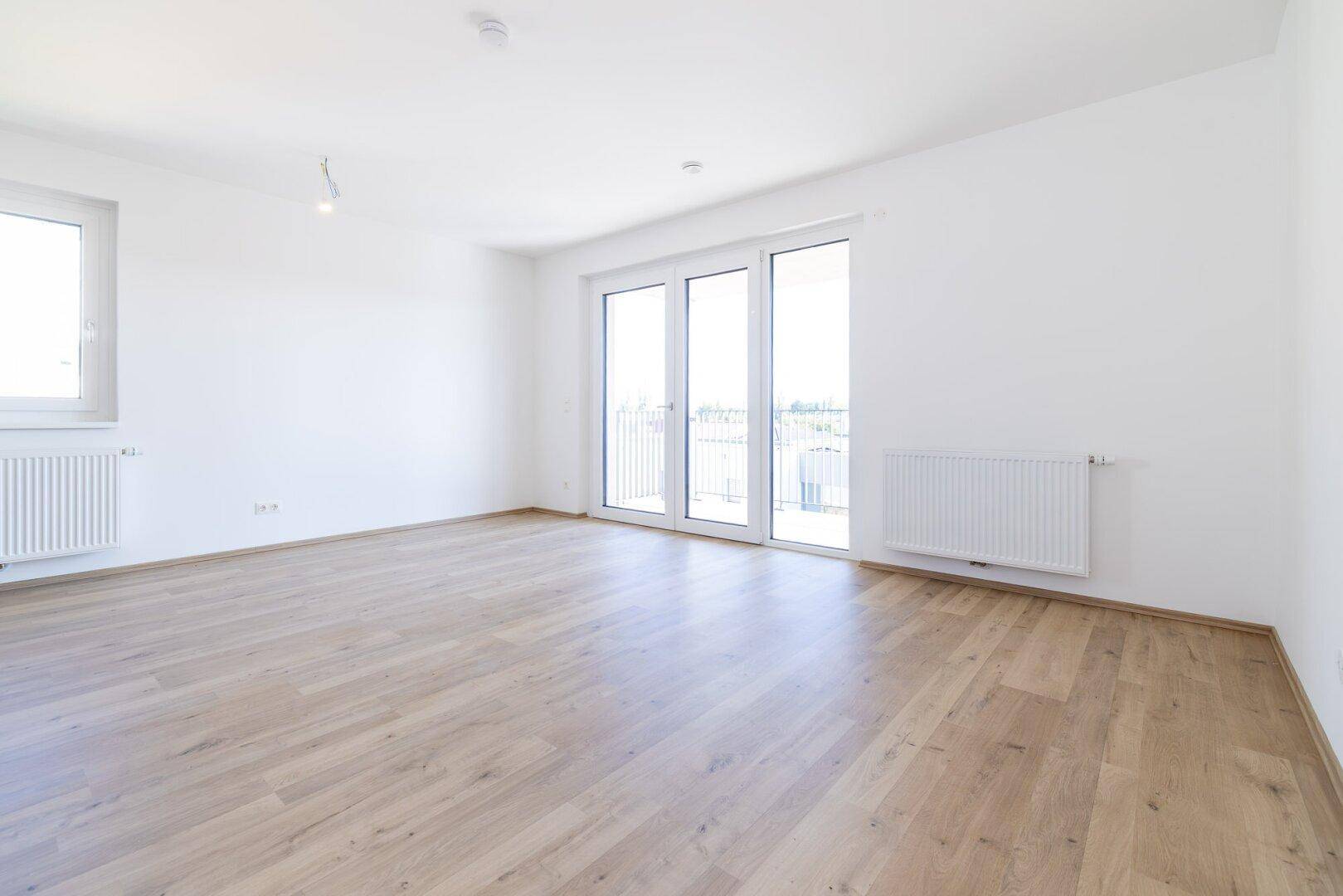 Lichtdurchfluteter Raum mit hellem Laminatboden und großen Fenstern, bereit zur individuellen Gestaltung.