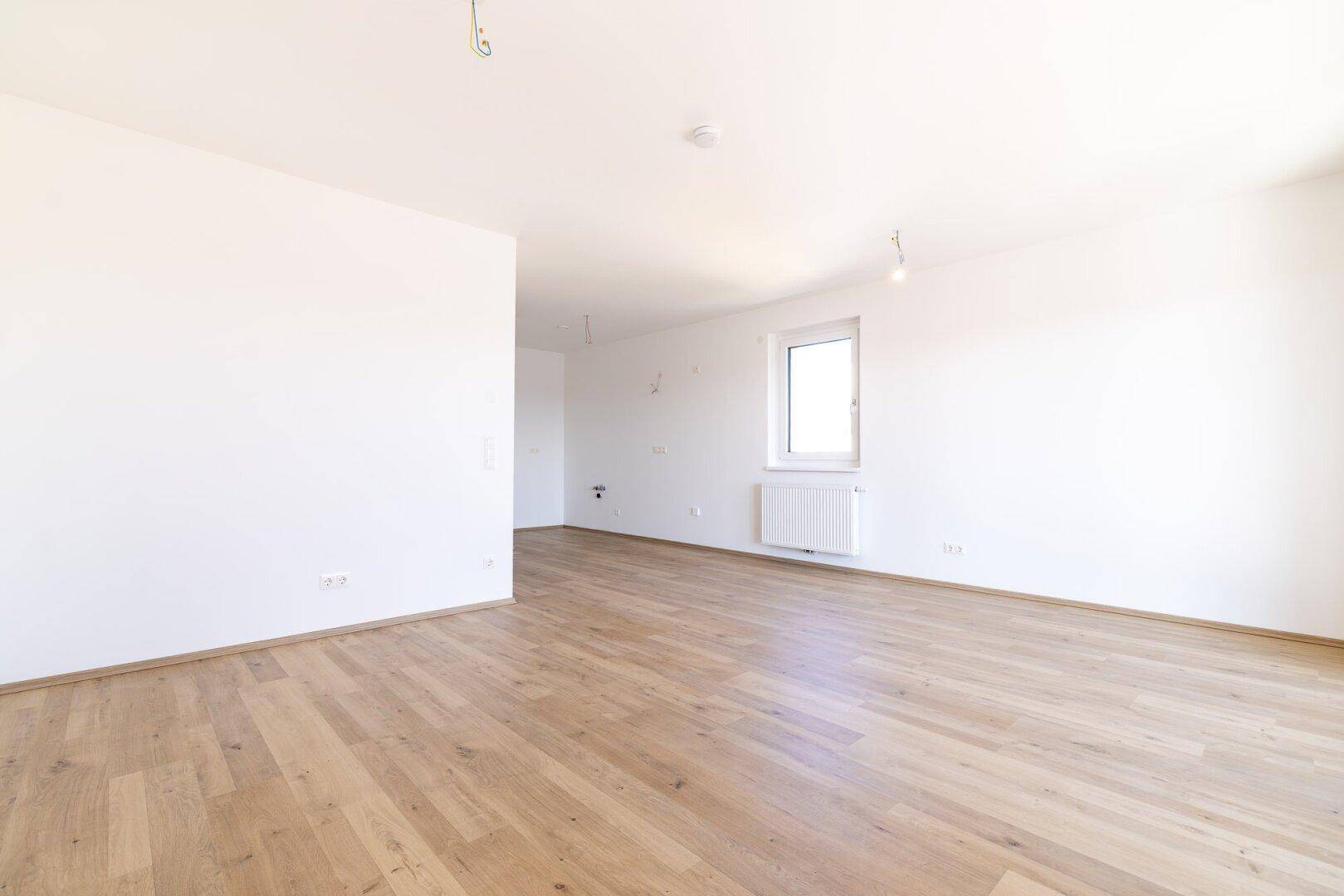Geräumiger, heller Raum mit Laminatboden und einem Fenster, ideal als Wohnbereich.