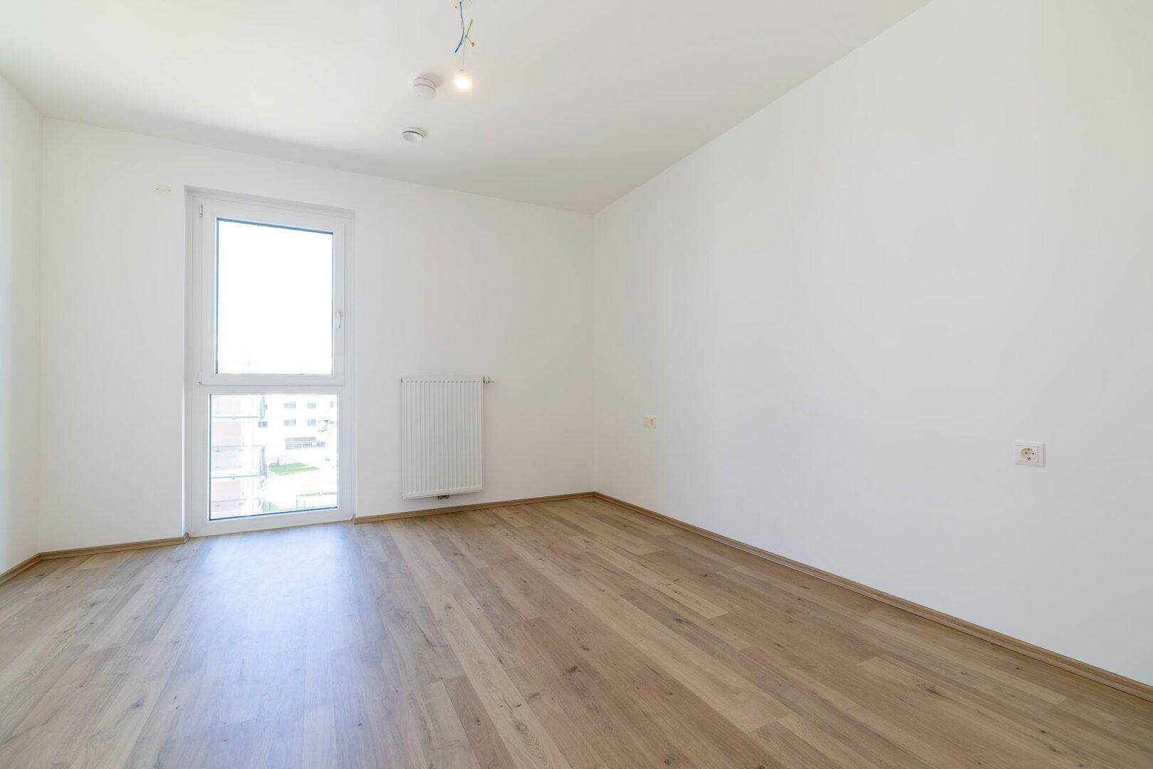 Heller Raum mit Laminatboden und Fenster, das einen Blick nach draußen ermöglicht.
