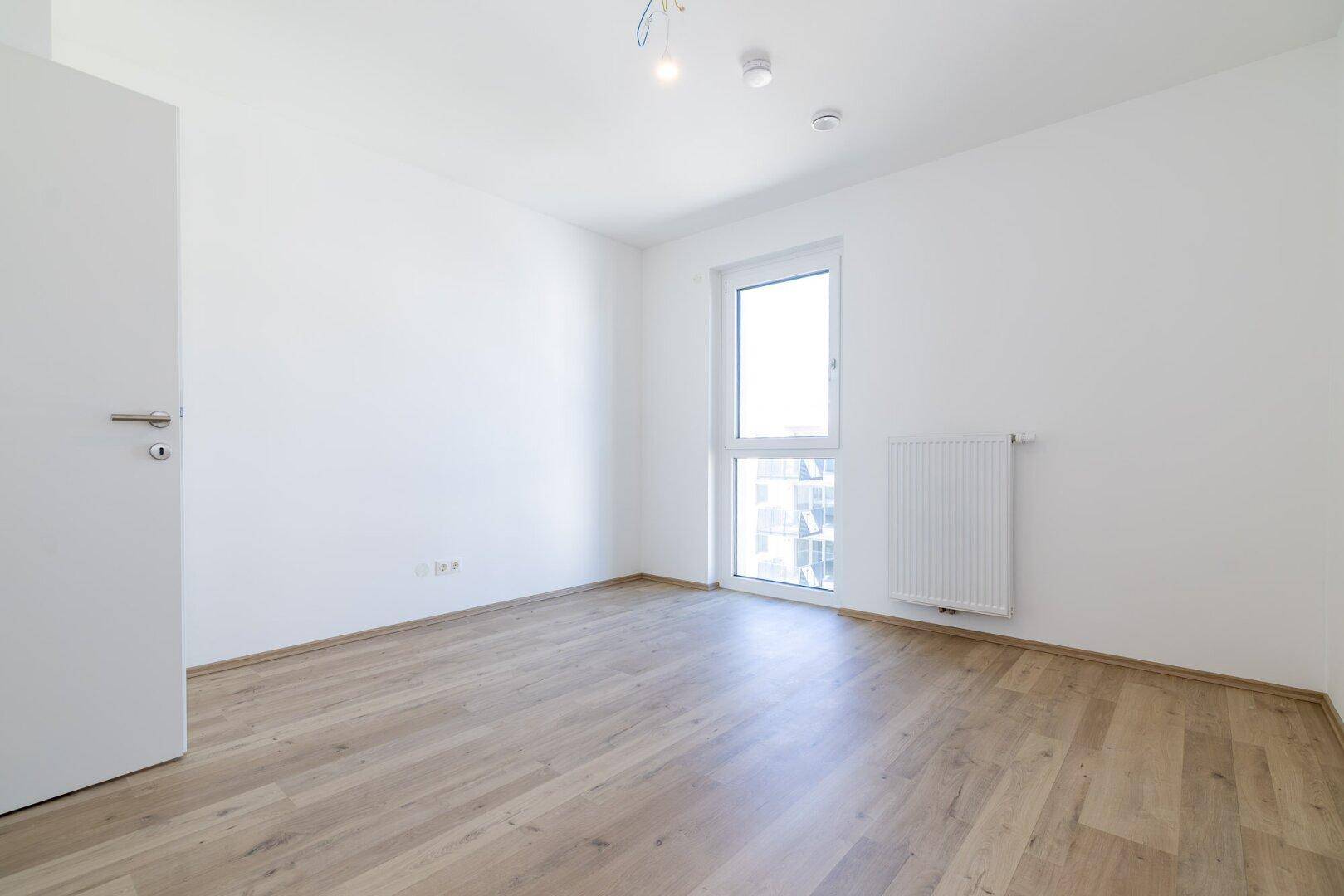 Geräumiges Zimmer mit Laminatboden und weißer Tür, ideal als Schlaf- oder Gästezimmer.