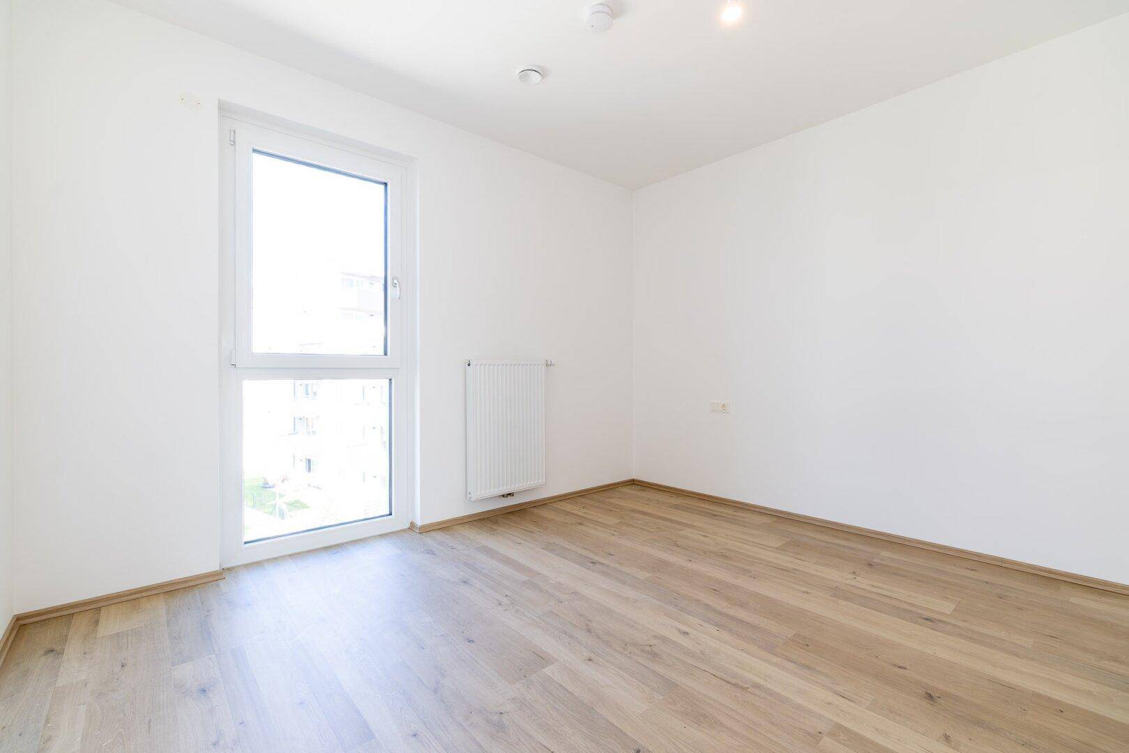 Helles Zimmer mit Laminatboden und großem Fenster, das viel Tageslicht bietet.