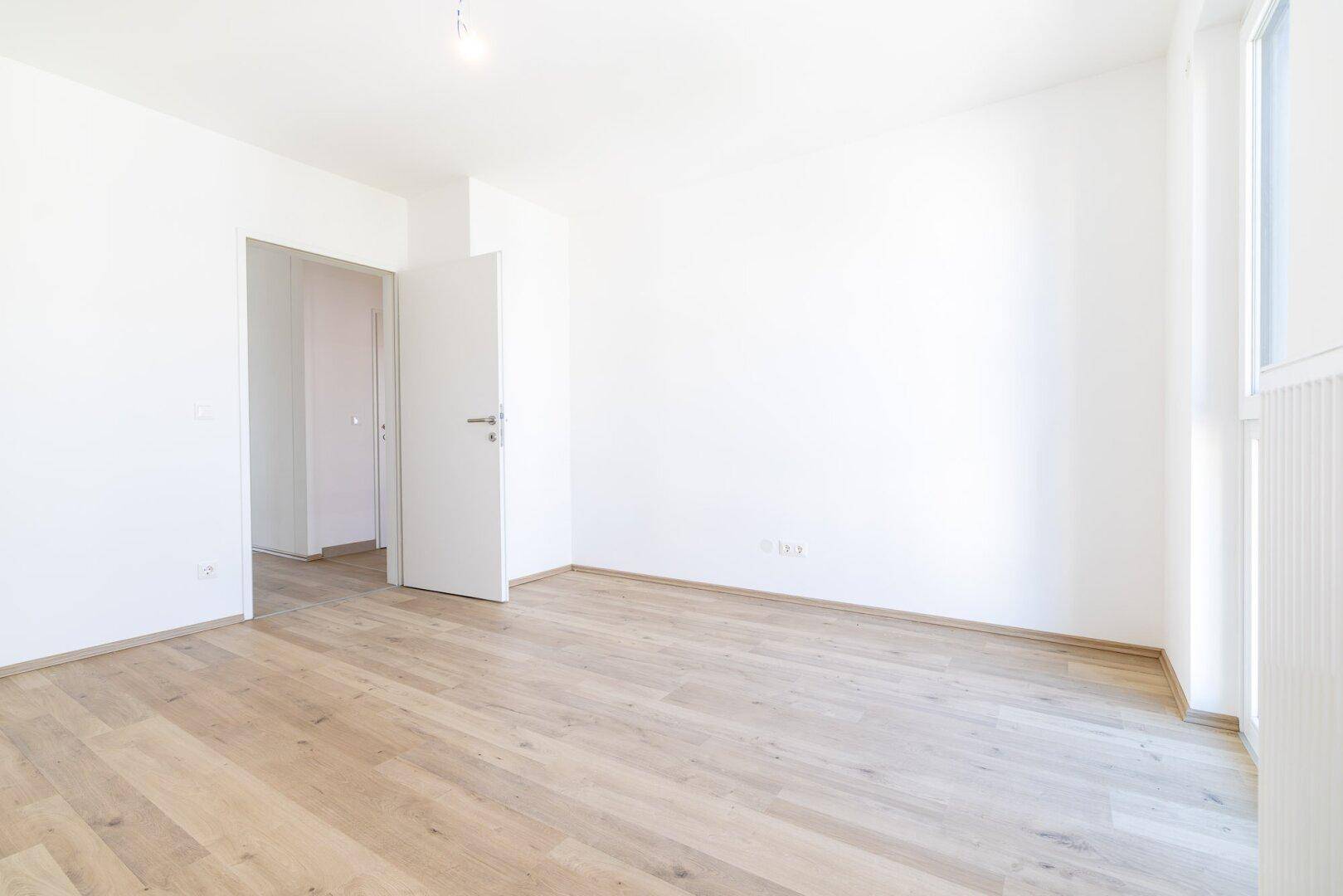 Leeres Zimmer mit Laminatboden und weißer Tür, bereit für die persönliche Einrichtung.