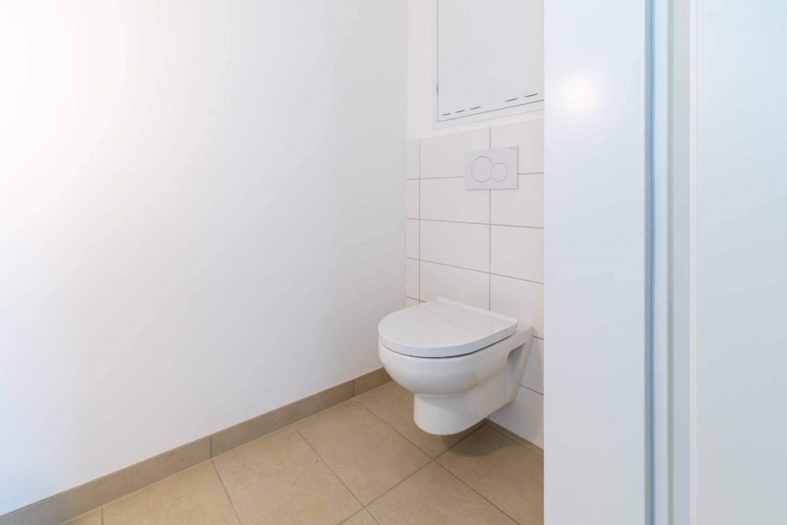 Separates WC mit Wand-WC und hellen Fliesen, funktional und sauber gestaltet.