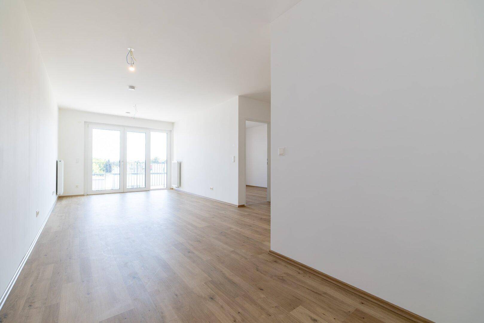 Großes, helles Wohnzimmer mit Laminatboden und Zugang zu einem sonnigen Balkon.