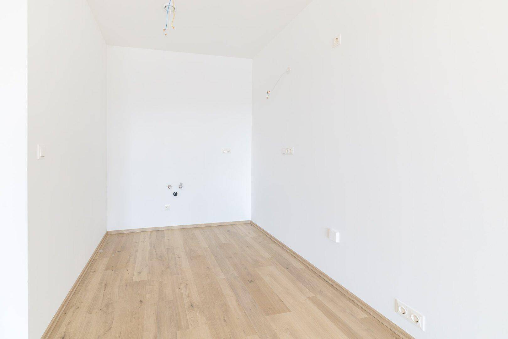 Kleiner, heller Raum mit Laminatboden und Anschlüssen für Wasserinstallationen.