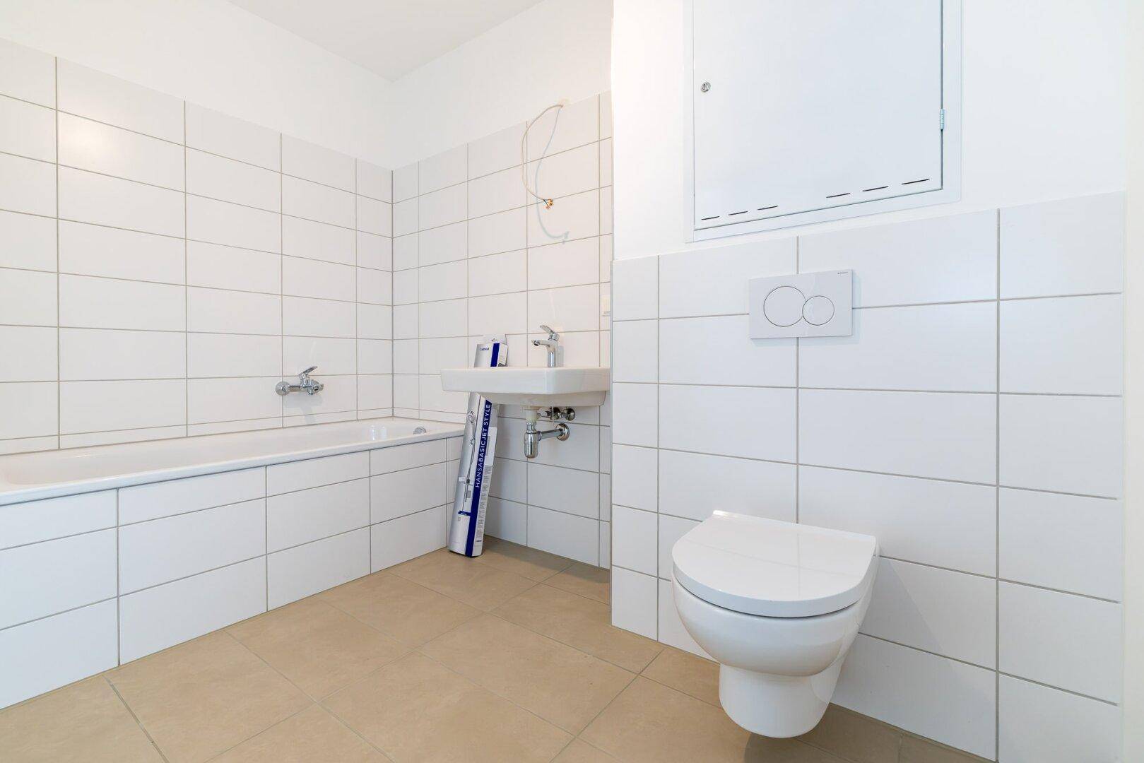 Helles Badezimmer mit weißen Fliesen, Badewanne und Wand-WC in neuwertigem Zustand.