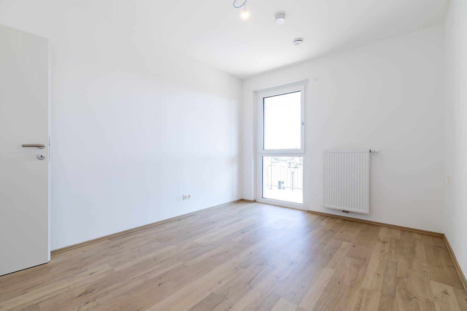 Unmöbliertes Schlafzimmer mit Laminatboden und weißer Tür, ideal für individuelle Gestaltung.